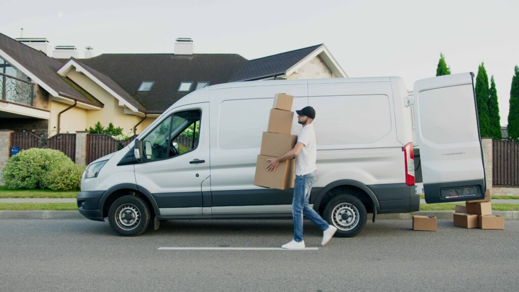Delivery driver holding packages beside a car, ready for on-time delivery.